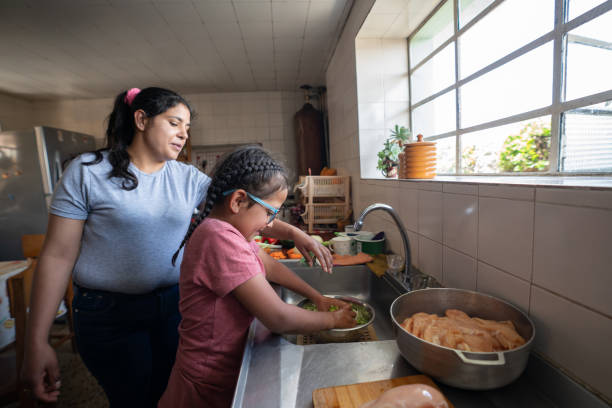 Latin American mother teaching her daughter to cook Latin American mother teaching her daughter to cook dinner at home - lifestyle concepts poverty stock pictures, royalty-free photos & images