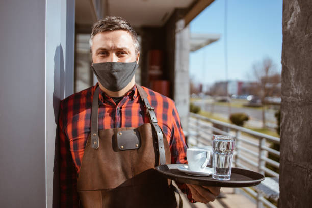 istock Waiter with protective face mask at the coffee shop door 1320063876