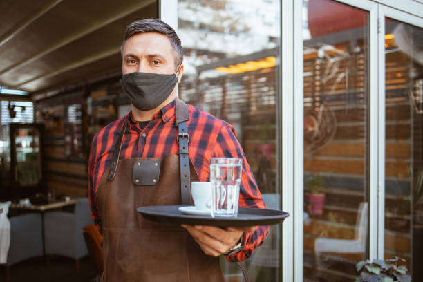 istock Waiter with protective face mask at the coffee shop door 1320063913