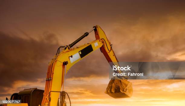 Backhoe Working By Digging Soil At Construction Site Closeup Hydraulic Arm And Bucket Of Backhoe With Scoop Of Soil Against Yellow Sunset Sky Excavator Digging On Dirt Trenching Machine Stock Photo - Download Image Now