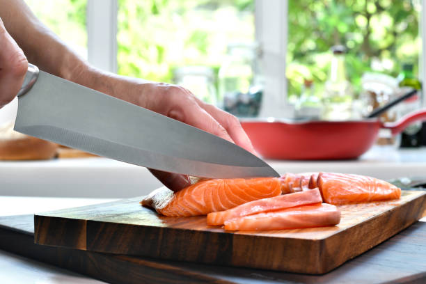 istock Hand slicing fresh raw salmon fillet steaks on a cutting board in the kitchen 1320077270