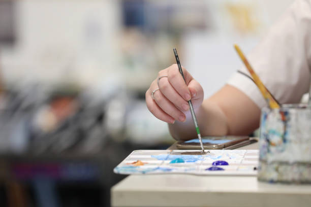 A student at a desk's hand mixing paint on a palette at a desk