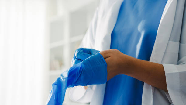 Young Asia lady doctor or nurse worker surgeon preparing for the surgical operation and wearing hand gloves at health clinic. Young Asia lady doctor or nurse worker surgeon preparing for the surgical operation and wearing hand gloves at health clinic or hospital office. Social distancing, quarantine for coronavirus. putting on latex gloves stock pictures, royalty-free photos & images