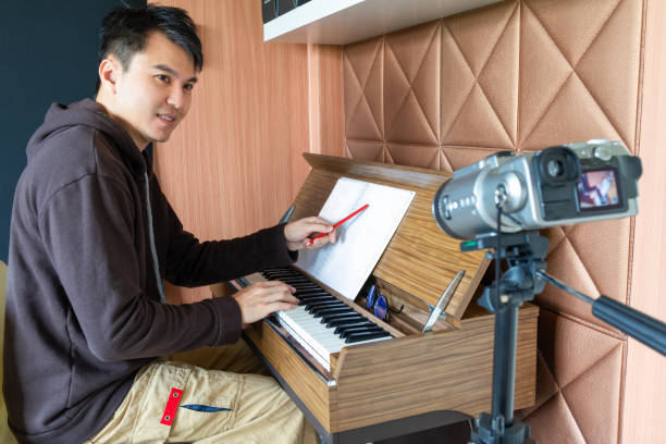 istock asian young handsome music instructor streaming a live video while teaching his student at home. e-learning technology concept 1320085975