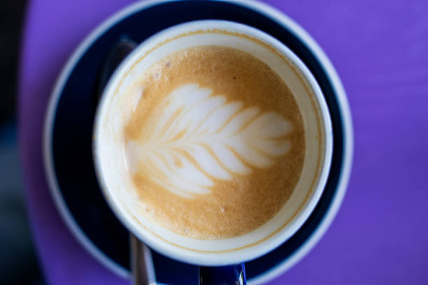 istock overflowing cup of latte coffee with drawn leaf on purple table, horizontal 1320094048