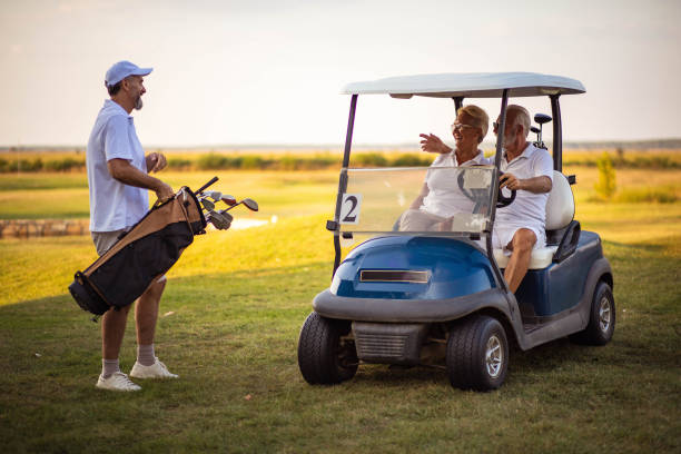 três jogadores de golfe. homem e mulher no carro de golfe. - senior couple golf retirement action - fotografias e filmes do acervo