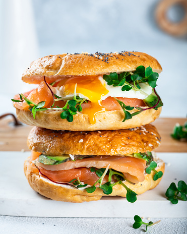 Healthy freshly baked bagel filled with salmon, microgreen, avocado and egg. Served on white desk. Sandwich with salmon. Healthy breakfast
