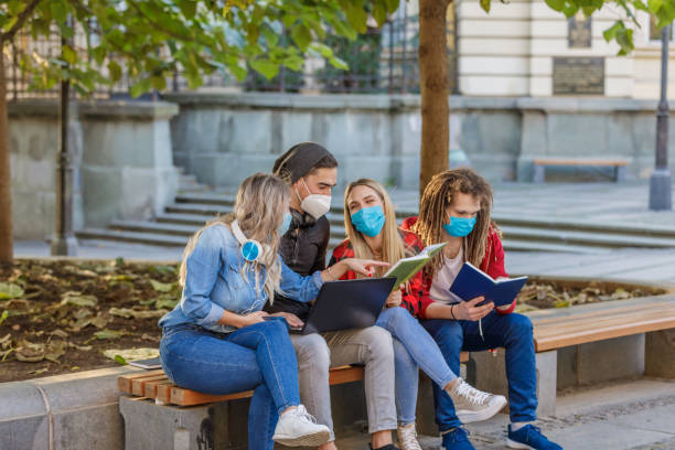 istock Beautiful Students are Working on a Laptop in Public Park with Preventive Measures due to Coronavirus. 1320104226