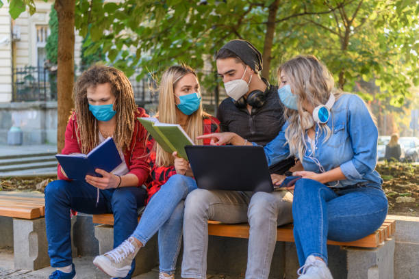 istock Handsome Group of Students in Shirts is Working on a Laptop in a Park with Protective Masks. 1320104719