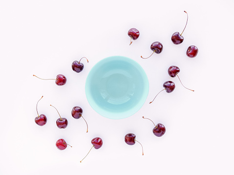 Ripe sweet cherry berries are scattered near an empty bowl on a green background. Natural sweets. Detox, healthy food concept. Flat lay. Top view. Copy space.