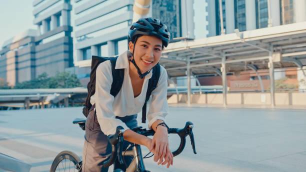 아시아 사업가가 사무실 스탠드에서 일하러 가서 도시를 짓는 거리에서 자전거를 타고 카메라를 바라보며 미소짓고 있습니다. - bicycle messenger 뉴스 사진 이미지
