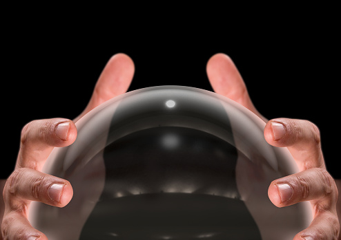 A close up of a pair of male hands surrounding a crystal ball on an isolated dark studio background