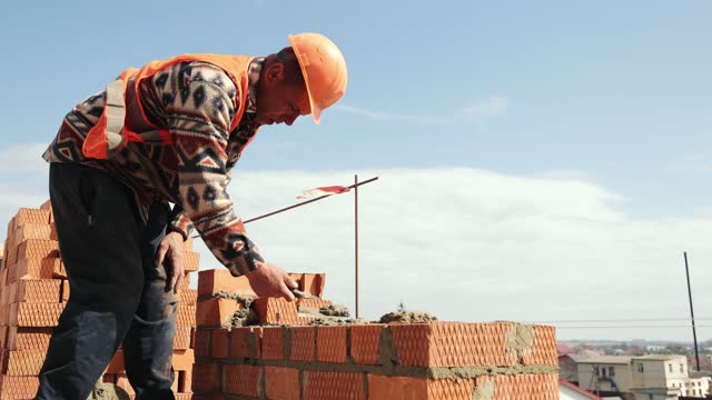 Close up of a man building a brick house. Laying red bricks on a construction site on a sunny day. House construction close up