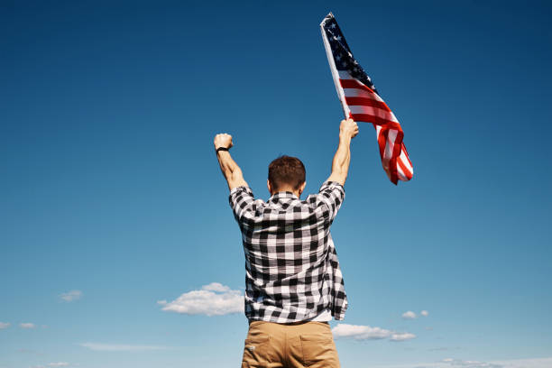 istock Man holds usa national flag against blue sky 1320108142