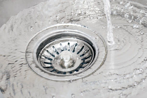 wasser, das aus dem wasserhahn in einem waschbecken läuft und mit siebstopper in den abfluss gießt. - colander stock-fotos und bilder