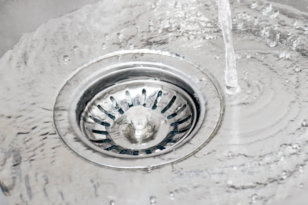 water running from tap in a sink and pouring into drain with strainer stopper. - colander imagens e fotografias de stock