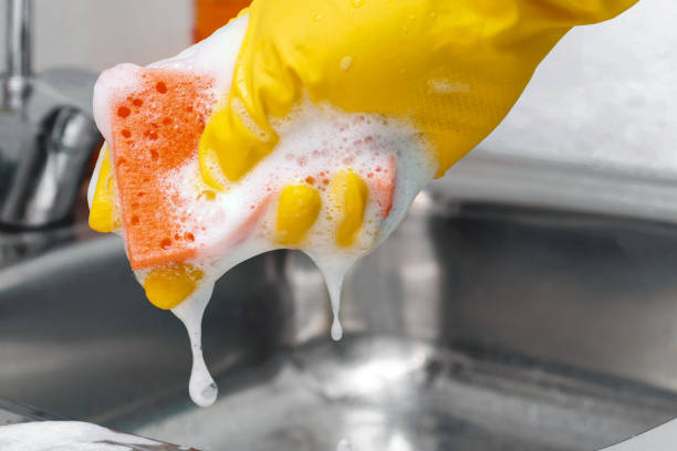 Hand in yellow latex protective glove squeezing out some foam from orange sponge. Hand in yellow latex protective glove squeezing out some foam from orange sponge. cleaning sponge stock pictures, royalty-free photos & images