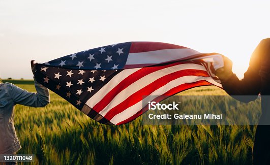 istock Hands holding American flag in a wheat field at sunset. Independence Day, 4th of July. 1320111048