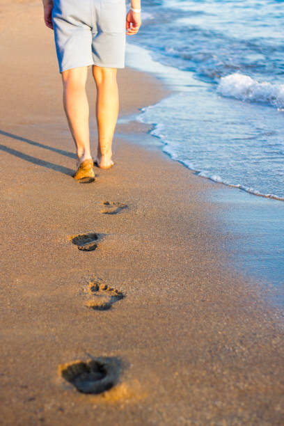 istock summer and vacation concept - walking man and footprints on the sunset beach 1320111221