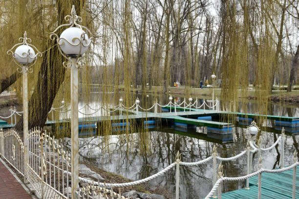 Willow branches bend over a pond with small green bridges and vintage lanterns in the park.