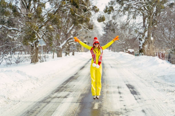 viaje. una mujer en un mono de esquí amarillo rebota contra el fondo de la carretera. - mono ski fotografías e imágenes de stock