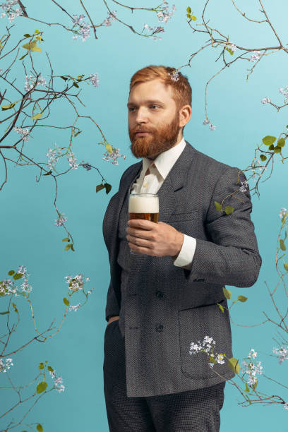 Portrait of young red headed and bearded man with glass of beer isolated over blue floral bacground Looking away. Portrait of young red headed bearded man playing famous artist Van Gogh isolated on blue bacground. Concept of art, beauty, eras comparison, fashion, fun, humor. Flowering branches. almond tree photos stock pictures, royalty-free photos & images