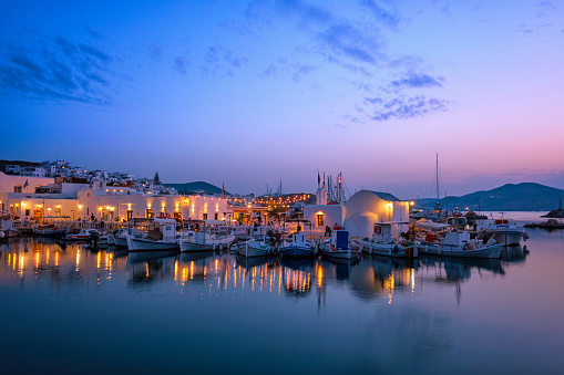 Picturesque view of Naousa town in famous tourist attraction Paros island, Greece with traditional whitewashed houses and moored fishing boats and seaside restaurants and cafe illuminated in night
