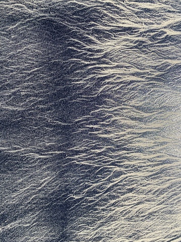 Black and beige ripples in the sand due to volcanic ash washing ashore on the beach