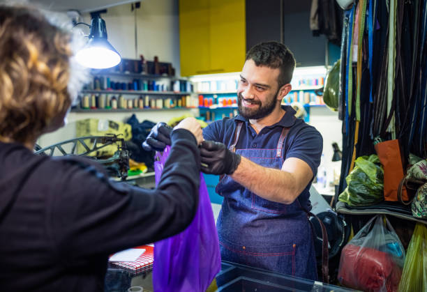 istock Smiling and giving plastic bag with repaired items to customer in workshop 1320124017