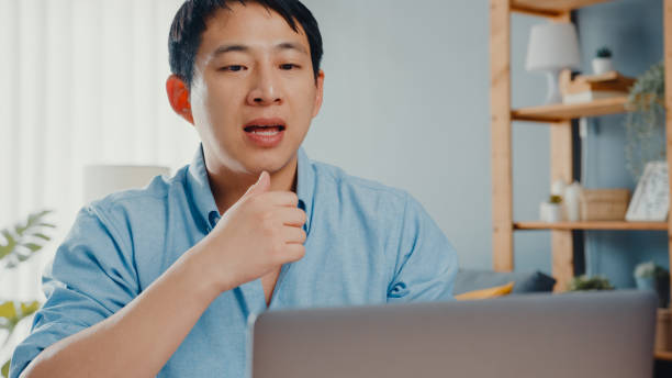 istock Young Asia businessman using laptop talk to colleagues about plan in video call while smart working from home at living room. 1320125498
