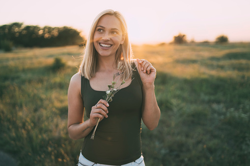 Beautiful young woman  and standing on a meadow at sunset