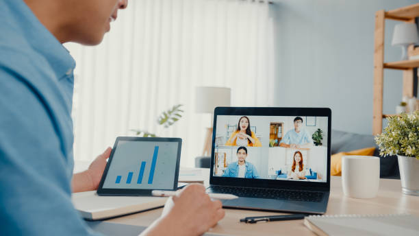 istock Young Asia businessman using laptop talk to colleagues about plan in video call meeting while work from home at living room. 1320125845