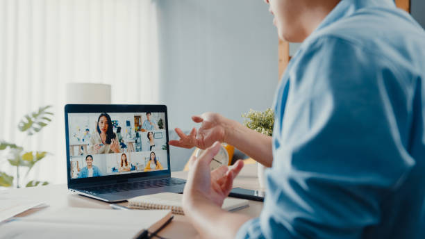 Young Asia businessman using laptop talk to colleagues about plan in video call meeting while work from home at living room.