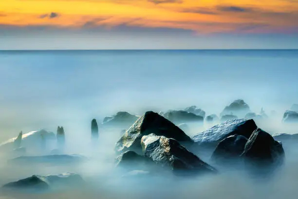 Photo of Seascape, water rolling over rocks at coastline mist long exposure scenic background.