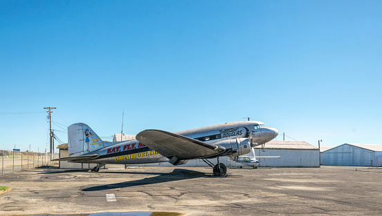 Lodi, California, USA - June 15, 2017: Antique Douglas DC-3 aircraft on the runway of an old airfield in Lodai, California, USA. The shiny fuselage of the plane against the background of hangars and a clear blue summer sky. History of American Aviation and Aircraft Engineering