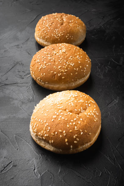 istock Fresh homemade burger buns with sesame, on black stone background 1320135480