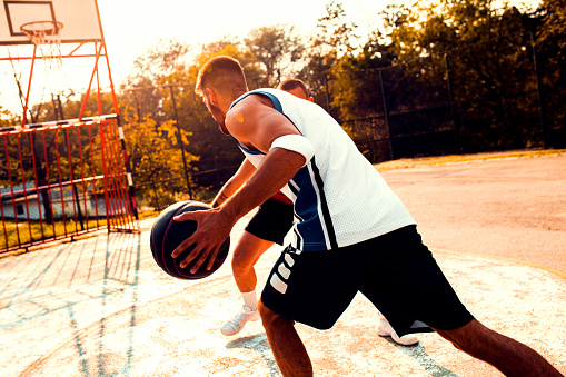 Two young friends playing basketball on court outdoors.