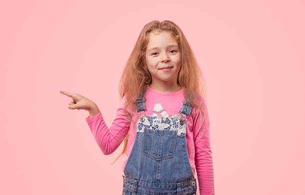 istock Smiling girl pointing away on pink background 1320137698