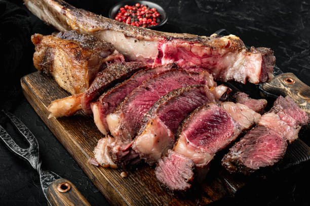 istock Grilled steak on the bone sliced, medium rare tomahawk cut, on wooden serving board, on black stone background 1320137789