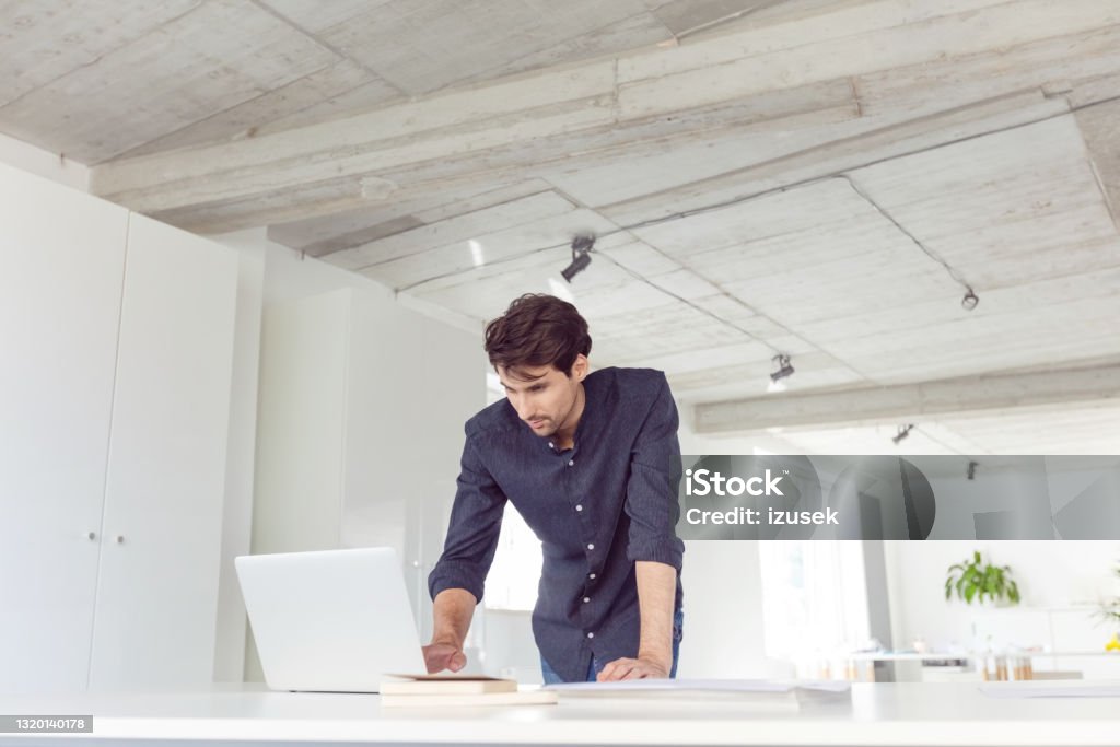Man in the office Mid adult men wearing dark shirt using computer in the modern white office. Man standing at the desk. Business Casual Stock Photo