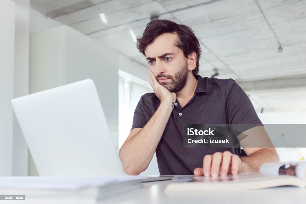 Man working in the office Thoughtful mid adult men wearing dark polo shirt using computer in the modern white office. Black Color Stock Photo