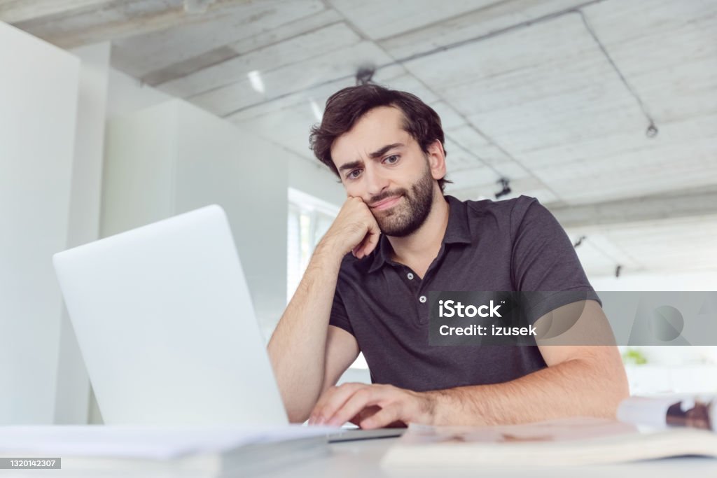 Man working in the office Thoughtful mid adult men wearing dark polo shirt using computer in the modern white office. Asking Stock Photo