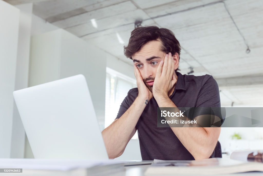 Overworked man in the office Tired mid adult men wearing dark polo shirt using computer in the modern white office. Men Stock Photo