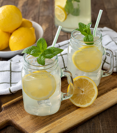 Two glasses of lemonade with lemon and mint on a rustic wooden table