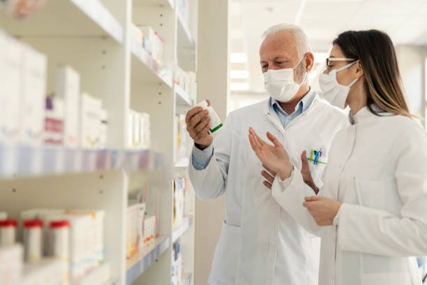 istock Pharmacist's recommendation and corona virus. Before retiring, the pharmacist explains to the young female pharmacist something about the recommendation of medication.They wear uniforms and face masks 1320144330