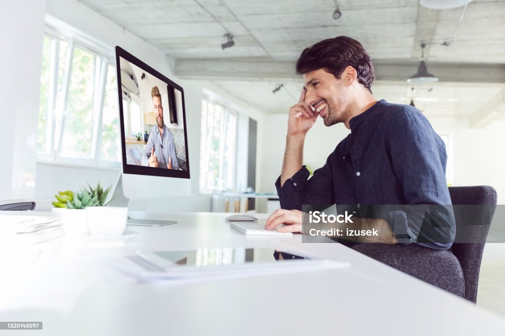 Man during video conference Happy mid adult men wearing dark shirt using computer in the modern white office, having video call. Desk Stock Photo