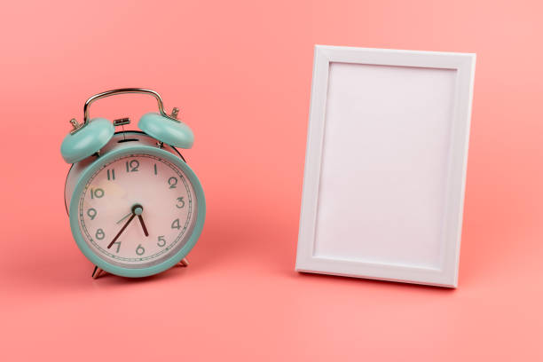 Vintage alarm clock and white photo frame on pink with copy space.