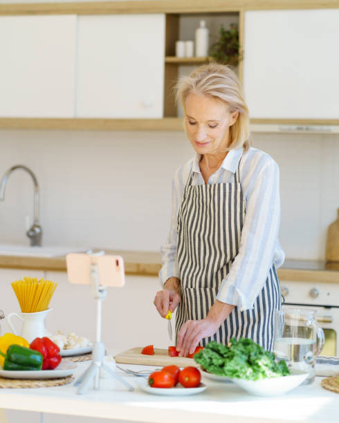 istock Eldrely female vlogger recording online culinary class or video recipe while cooking at home in modern kitchen 1320146421