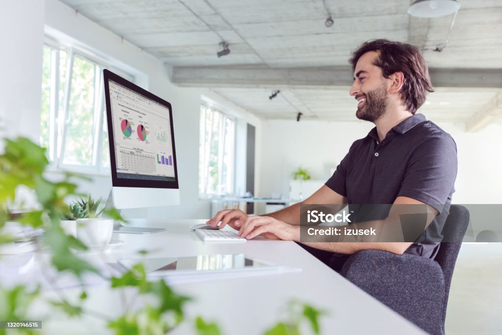 Man working in the office Happy mid adult men wearing dark polo shirt using computer in the modern white office. Computer Monitor Stock Photo