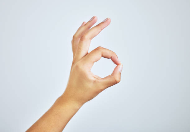 projectile de studio d’une femme faisant un signe « a-ok » avec sa main sur un fond gris - doigts en forme de o photos et images de collection